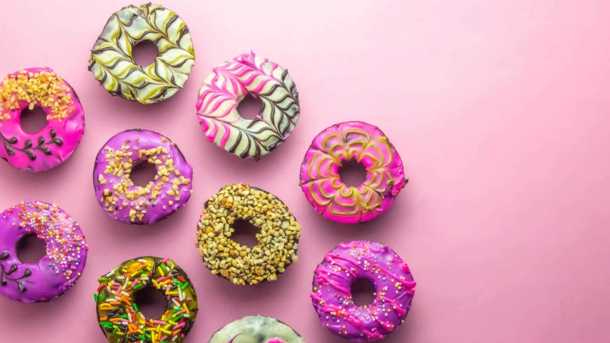 An assortement of beautiful decorated donuts on a pink table. Photo is an ariel view.